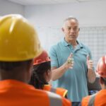 A workplace supervisor discusses the safety plan while members of his crew listen and take notes.